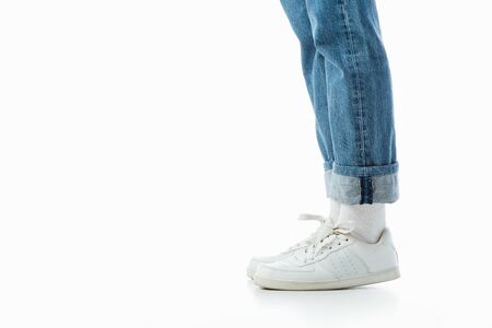 cropped view of teenage girl legs in white sneakers and blue jeans isolated on white