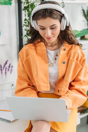 pretty smiling girl listening music in headphones and using laptop at home