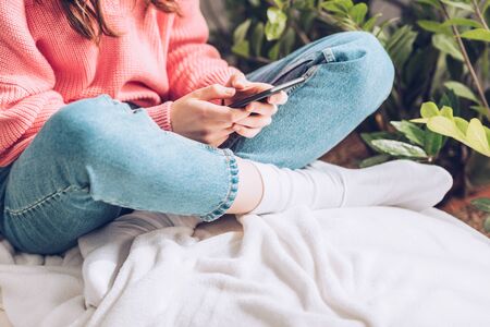 cropped view of girl sitting with crossed legs and using smartphoneの写真素材