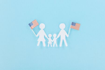 top view of  paper cut family holding decorative american flags on wooden sticks on blue backgroundの写真素材