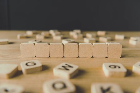 selective focus of seven blank cubes surrounded by blocks with letters on wooden surface isolated on blackの写真素材