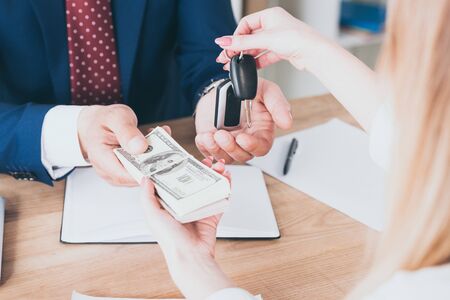 cropped view of business man taking dollar banknotes from customer holding car keysの写真素材