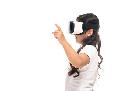 side view of latin kid pointing with finger while wearing virtual reality headset isolated on whiteの写真素材