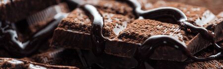 Panoramic shot of pieces of chocolate bar with melted chocolate