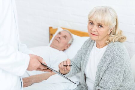 cropped view of doctor with clipboard, senior woman and ill patientの写真素材