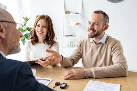 Happy man gesturing near woman with clipboard and car dealerの写真素材