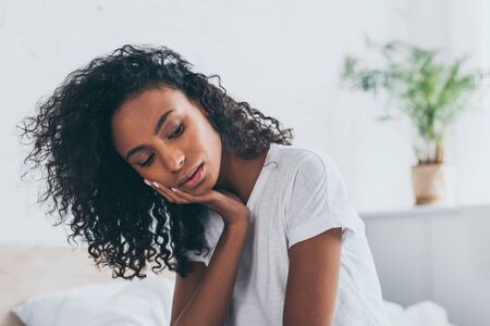 Sad African American woman suffering from tooth pain in bedroomの写真素材