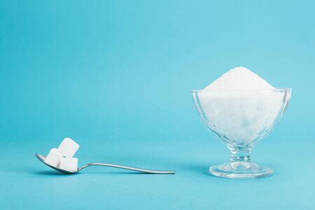 Glass bowl with granulated sugar and teaspoon with sugar cubes on blue background with copy spaceの写真素材