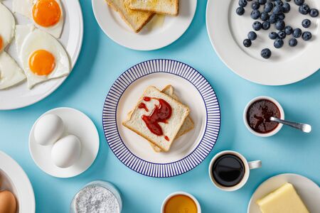 Top view of table setting for breakfast and toasts with jam on plates on blue backgroundの写真素材