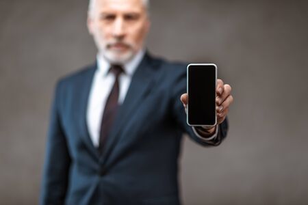 Selective focus of businessman holding smartphone with blank screen on grey backgroundの写真素材