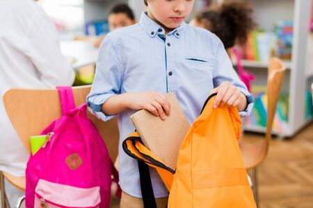 Cropped view of kid standing and putting book in backpackの写真素材