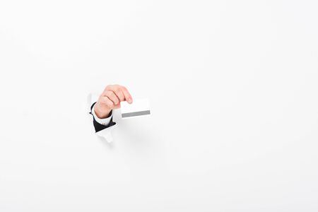 Cropped view of man holding Credit card from hole in wall on white background with copy spaceの写真素材