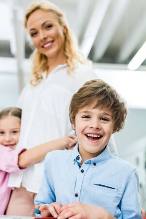 Selective focus of cheerful kid smiling while looking at camera near womanの写真素材
