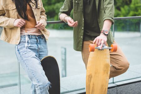 Cropped view of man and woman standing with skateboard on green trees backgroundの写真素材