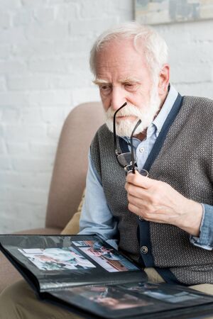 Calm senior man holding photo album and glasses in handsの写真素材