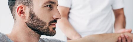 Panoramic shot of chiropractor stretching arm of handsome patient in hospitalの写真素材