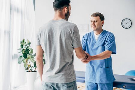Back view of patient shaking hands with doctor in massage cabinet at clinicの写真素材