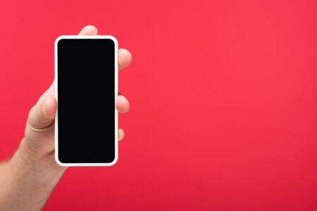 Cropped view of man holding smartphone with blank screen isolated on pink backgroundの写真素材