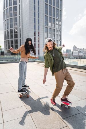 Happy man with beautiful woman riding on skateboards on roofの写真素材