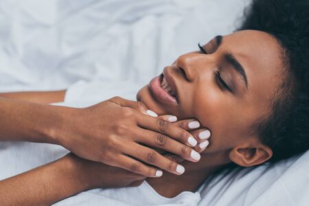 Pretty African American woman suffering from tooth pain while lying in bed