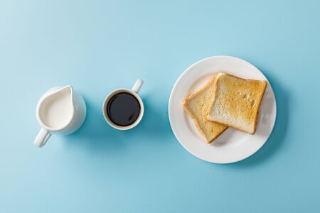 Top view of milk, two toasts on white plate and cup of coffee on blue backgroundの写真素材