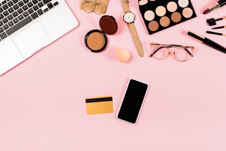 Top view of laptop, smartphone with blank screen, credit card and decorative cosmetics on pink backgroundの写真素材