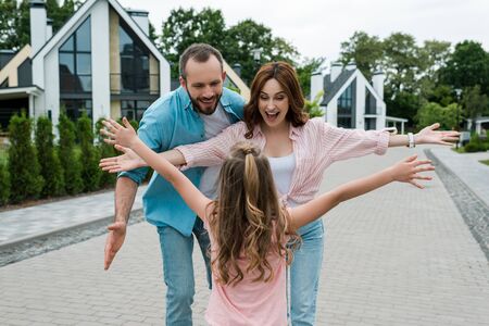 Back view of kid with outstretched hands standing near happy parentsの写真素材