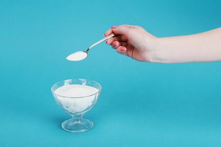 Cropped view of woman adding granulated sugar into glass bowl on blue backgroundの写真素材