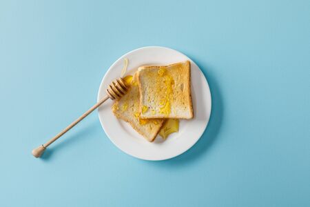Top view of toasts with honey and wooden dipper on white plate on blue backgroundの写真素材