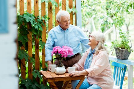Selective focus of happy senior man looking at retired wife sitting near cupsの写真素材