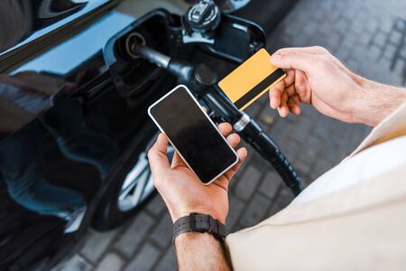 Cropped view of man holding credit card near smartphone with blank screen
