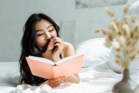 Selective focus of Asian girl with duck face touching hair while reading bookの写真素材