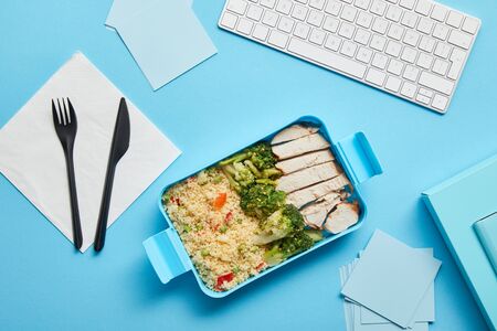 Top view of lunch box with delicious rice with chicken and broccoli at workplace with computer...