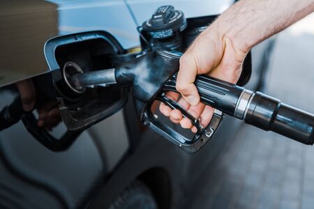 Cropped view of man holding fuel pump and refueling car at gas stationの写真素材