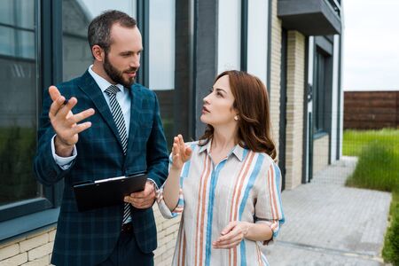 Handsome bearded broker holding clipboard and gesturing near womanの写真素材