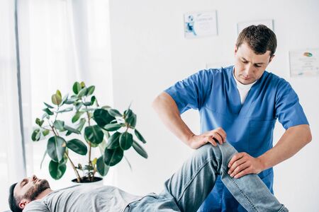 Handsome Physiotherapist massaging leg of patient in hospitalの写真素材