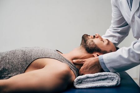 Chiropractor massaging neck of handsome man lying on Massage Table on grey backgroundの写真素材