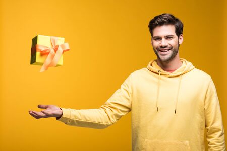 Handsome smiling man throwing in air gift on yellow backgroundの写真素材