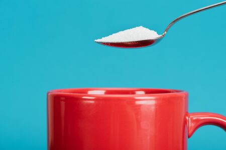 Teaspoonful of granulated sugar near red cup isolated on blue backgroundの写真素材