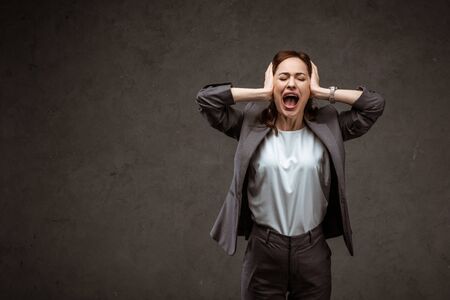 Brunette woman standing and touching head while screaming on grey backgroundの写真素材
