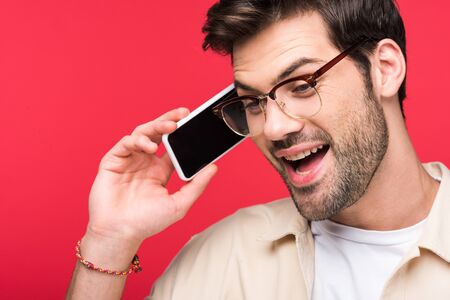 Excited man talking on smartphone isolated on pink background