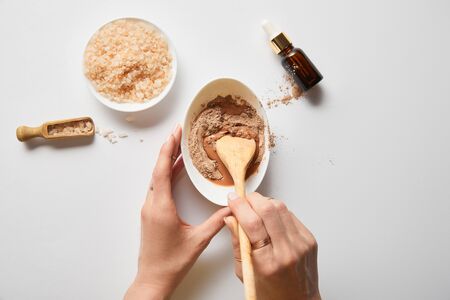 Cropped view of woman mixing clay in bowl with wooden spoon near sea salt and oil on marble tableの写真素材