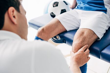 Partial view of Physiotherapist massaging leg of football player in hospitalの写真素材