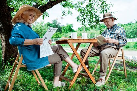 Senior woman reading travel newspaper near husband with bookの写真素材