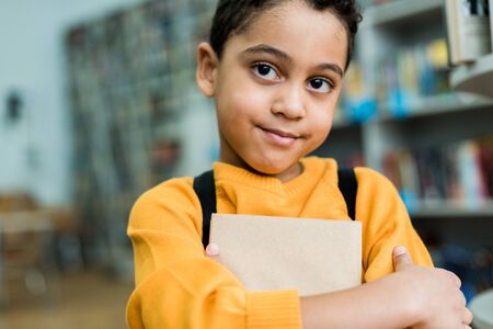 Adorable African American kid holding book and looking at cameraの写真素材