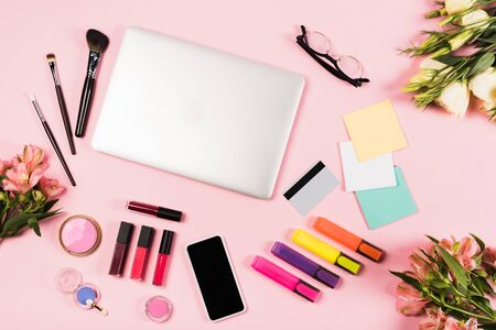 Top view of laptop, smartphone with blank screen, credit card, flowers, glasses, highlighters and...
