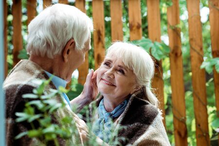 Selective focus of senior man with grey hair touching face of retired wife