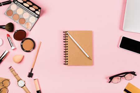 Top view of notebook with pencil, glasses, smartphone with blank screen, credit card, accessories and decorative cosmetic on pink backgroundの写真素材
