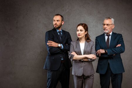 Successful businesswoman and handsome businessmen standing with crossed arms on grey backgroundの写真素材