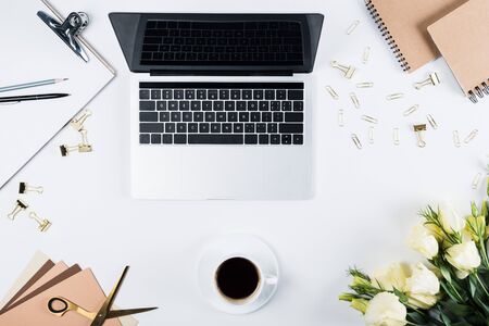 Top view of laptop with blank screen, cup of coffee, clipboard, flowers, pen, pencil, scissors, binder clips and paper clips of white backgroundの写真素材